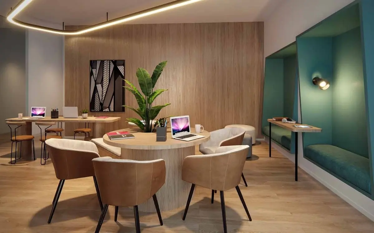 O coworking com mesas redondas, notebooks abertos e uma cabine estofada em verde.