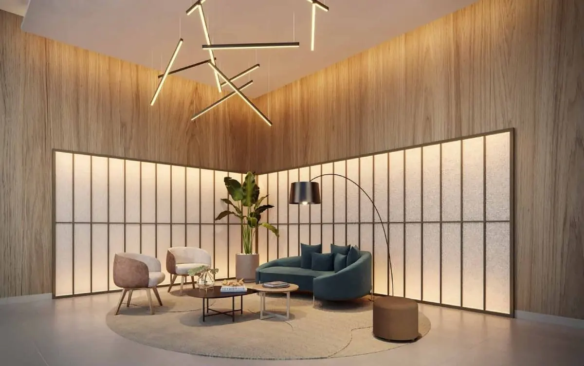 O lobby com pé-direito alto, poltronas, um lustre de hastes e uma parede de vidro iluminada.