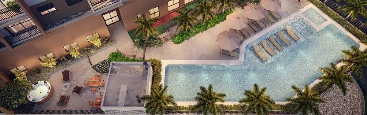 O lazer visto do alto: a piscina em L entre palmeiras, o solário com espreguiçadeiras e o deck ao lado.