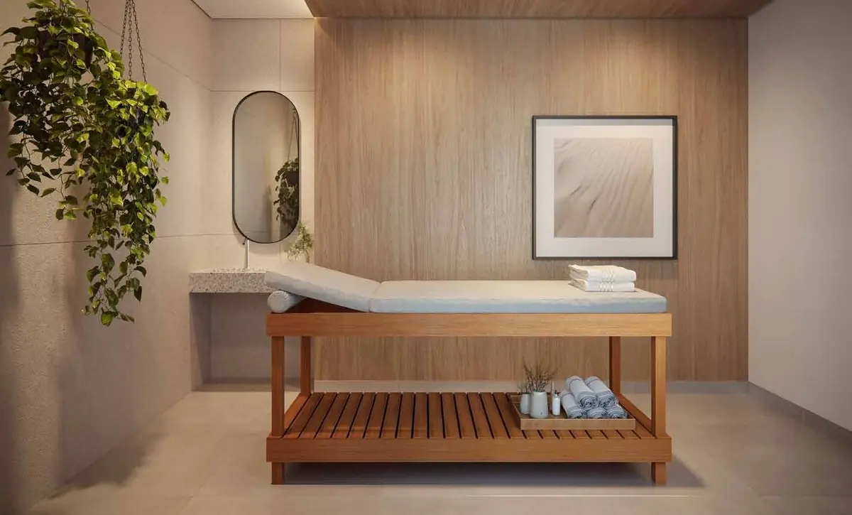 A sala de massagem com a maca de madeira, um espelho oval e plantas penduradas.