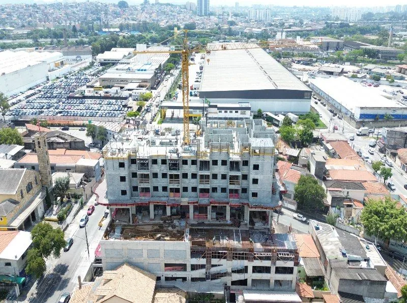 A torre em obra, de lado, com a grua e os galpões do bairro ao fundo.