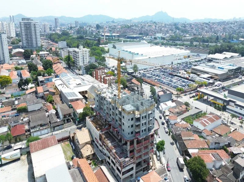 A torre em obra vista de longe, entre as casas do bairro, com os morros no horizonte.