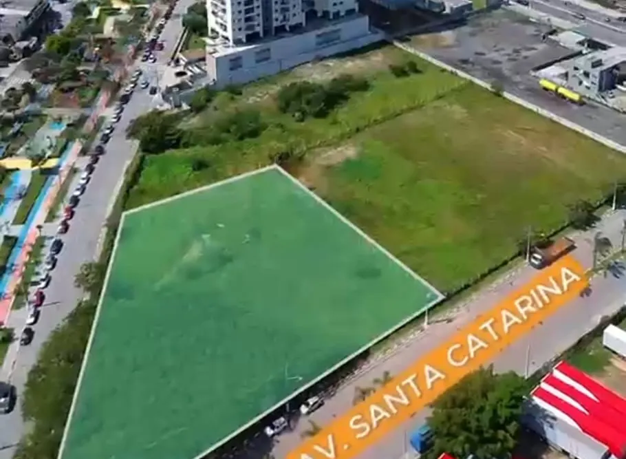 Foto aérea do terreno vazio e gramado, contornado em verde, na esquina da Avenida Santa Catarina, com o pé de uma torre vizinha ao fundo.