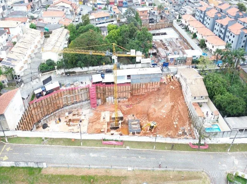 O terreno da obra visto do alto, com a contenção nas bordas, a grua e as casas do bairro em volta.