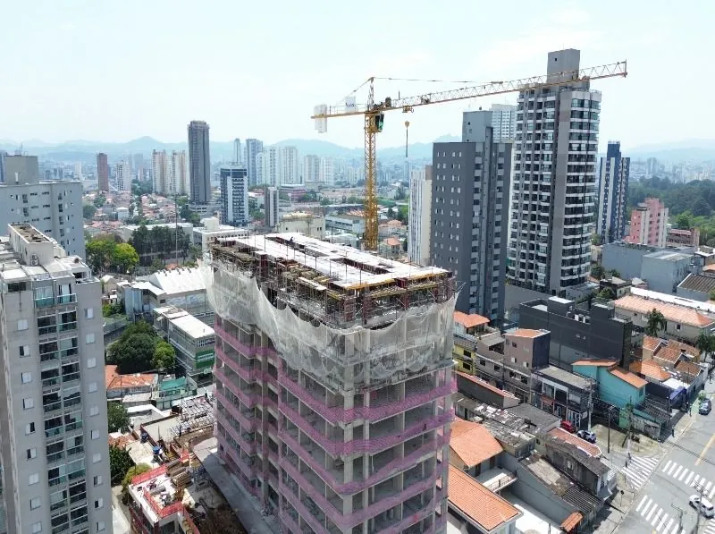 A torre em obra de corpo inteiro, com as telas de proteção e a grua ao lado.